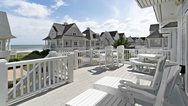 A coastal property with a wooden deck, white railings, and multiple houses with gabled roofs. - Aqua Vista #174 - Private Hot Tub, Community Pool, Dog Friendly! (North Topsail Beach)