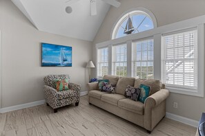 A living room with a beige sofa, patterned armchair, and a painting of a sailboat.