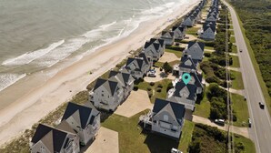 A coastal residential area with houses aligned along a beachfront, featuring a road and a beach in the background. - Aqua Vista #174 - Private Hot Tub, Community Pool, Dog Friendly! (North Topsail Beach)