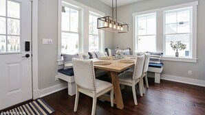 A dining area with a wooden table and white upholstered chairs, large windows, and a hanging light fixture. - Newer luxury cottage with hot tub; walking distance to town and beach (New Buffalo)