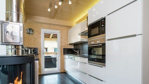 A modern kitchen with a wood-burning stove, stainless steel appliances, and a view to an outdoor deck. - Majestic Chalet With Sauna (Sankt Georgen am Kreischberg)