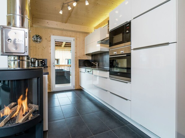 A modern kitchen with a wood-burning stove, stainless steel appliances, and a view to an outdoor deck. - Majestic Chalet With Sauna (Sankt Georgen am Kreischberg)