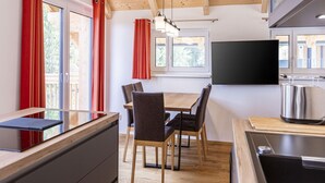 A modern kitchen with wooden beams, a dining area with a table and chairs, and a TV mounted on the wall. - Inviting Chalet on the Ski-slope (Stadl-Predlitz)