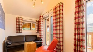 A modern living room with a black leather sofa, a wooden side table, and a red chair. The room has plaid curtains and a view of a balcony. - Spacious Apartment With Terrace (Stadl-Predlitz)