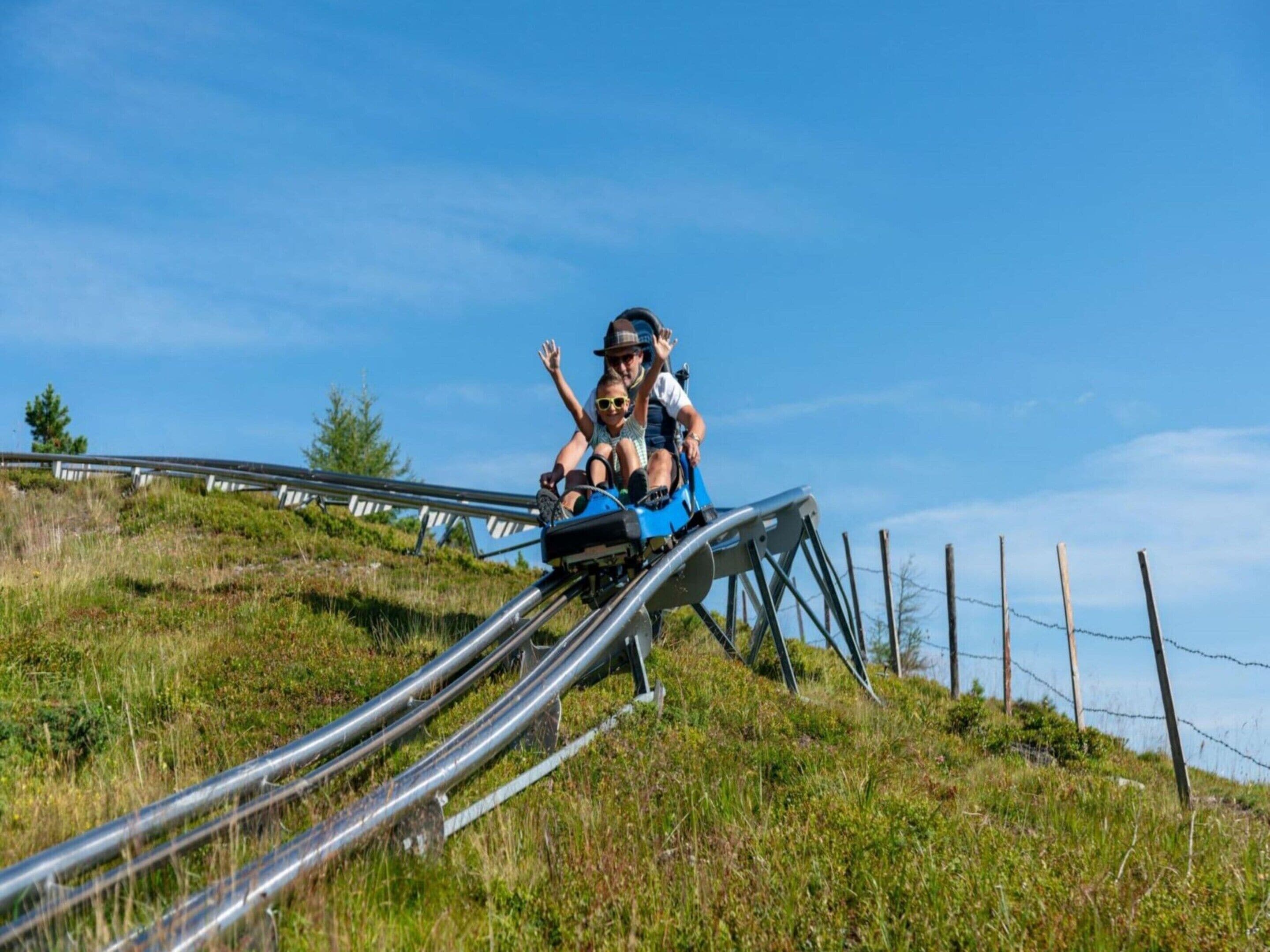 A person on a blue sled-like vehicle on a metal track with a grassy hill and a clear blue sky in the background.