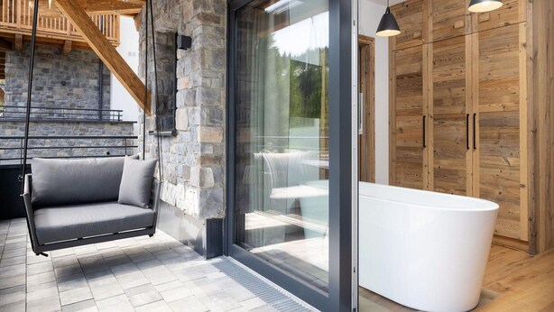 A modern interior with a stone wall, a glass door leading to a balcony, a white bathtub, and wooden cabinets. - Attractive Chalet on the Ski-slopes (Stadl-Predlitz)