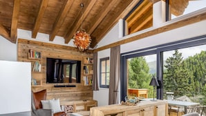 A cozy living room with a wooden ceiling, a flat-screen TV, bookshelves, and a view of the outdoors. - Attractive Chalet on the Ski-slopes (Stadl-Predlitz)