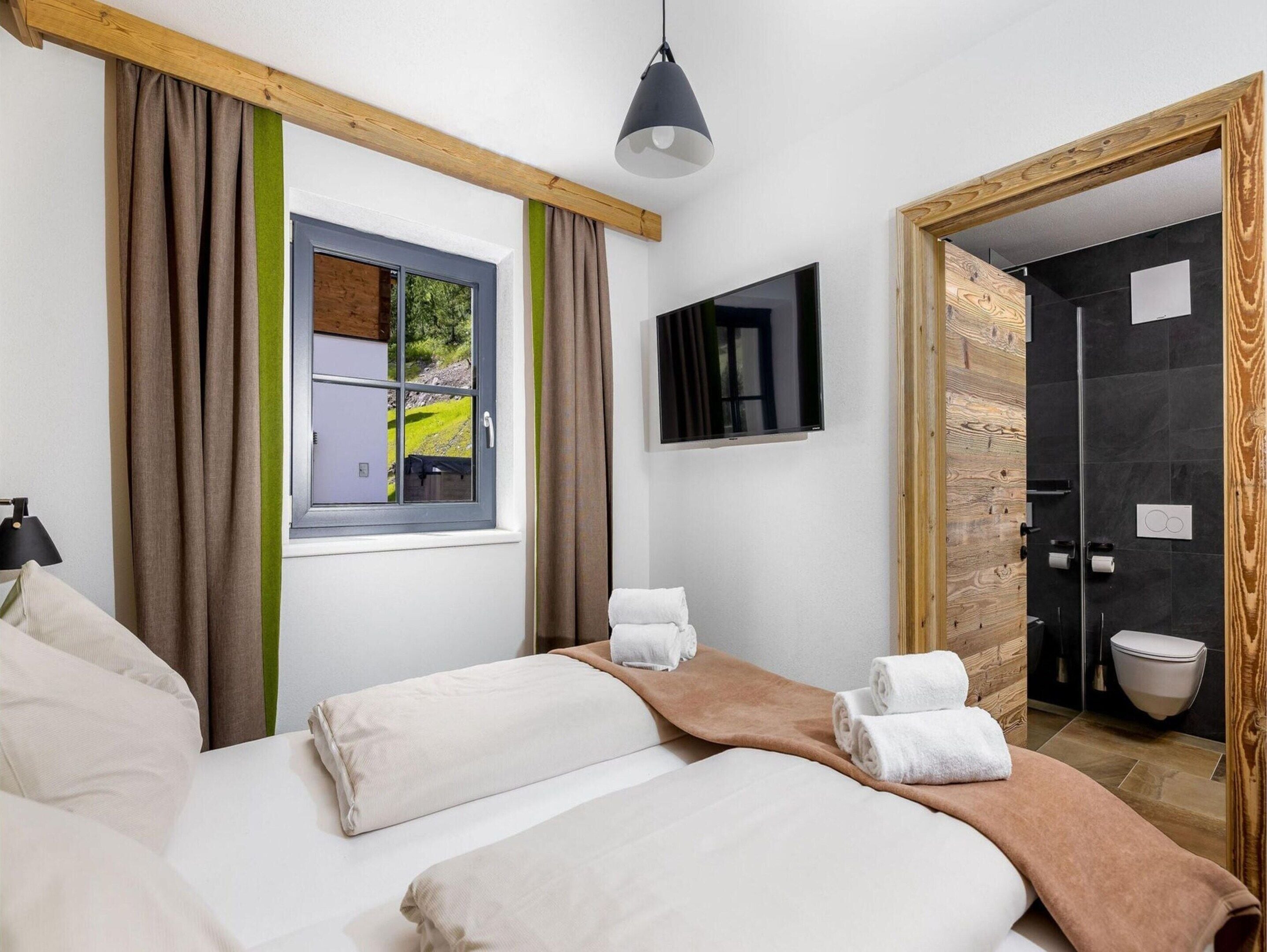 A hotel room with a bed, a window with curtains, a television, and a bathroom visible through an open door.