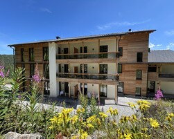 Un edificio de varios pisos con fachada de madera, balcones y un jardín con flores amarillas.