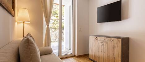 Un salon comprenant un canapé, un téléviseur fixé au mur et une porte-fenêtre coulissante donnant sur un espace extérieur.