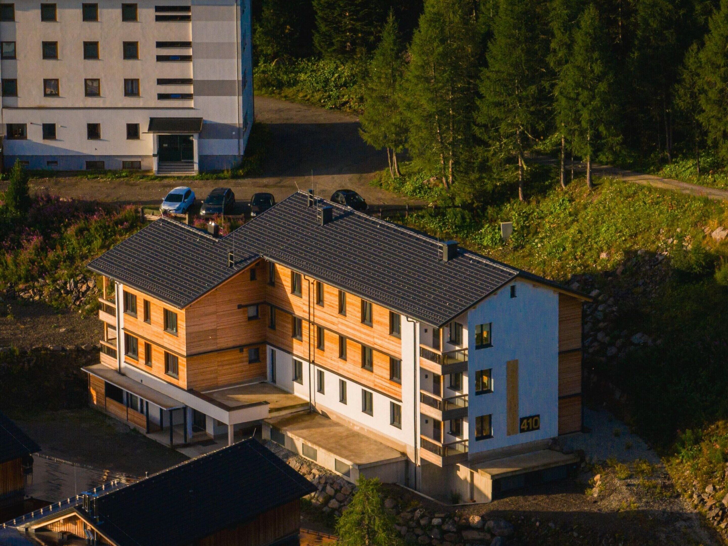 A multi-story building with a modern design, featuring a mix of wooden and white exterior panels, and a sloped roof.