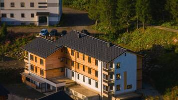A multi-story building with a modern design, featuring a mix of wooden and white exterior panels, and a sloped roof.