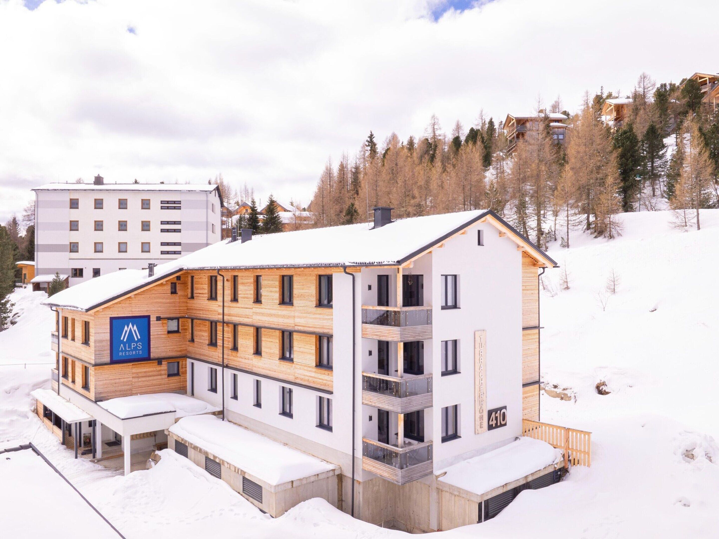 Un edificio moderno con el logotipo de una estación de esquí, varios balcones y suelo cubierto de nieve.