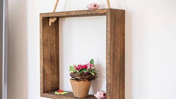 A rustic wooden frame with a woven basket containing pink flowers and green foliage, hanging on a white wall.