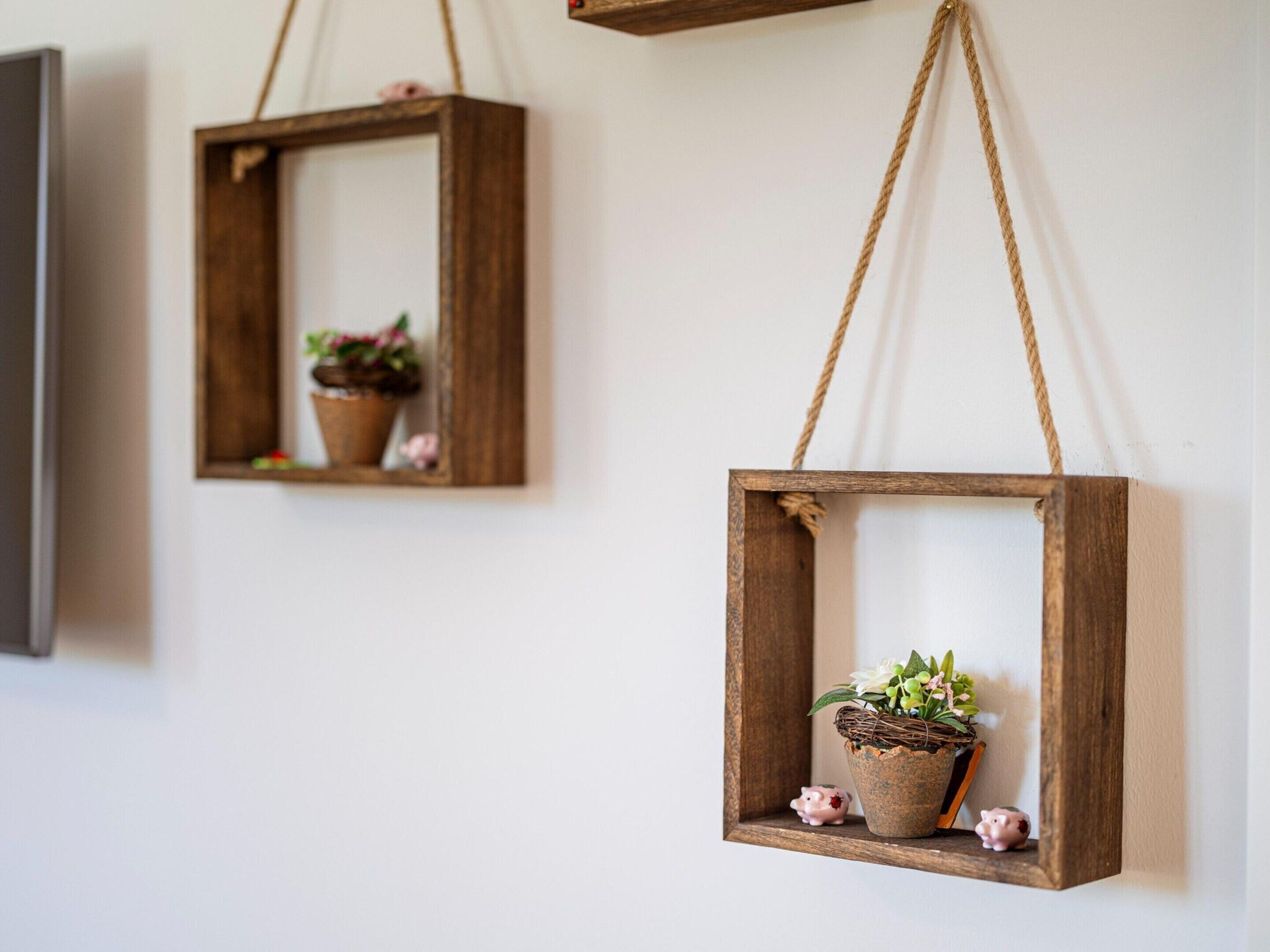 Two wooden hanging planters with plants and small pig figurines on a white wall.