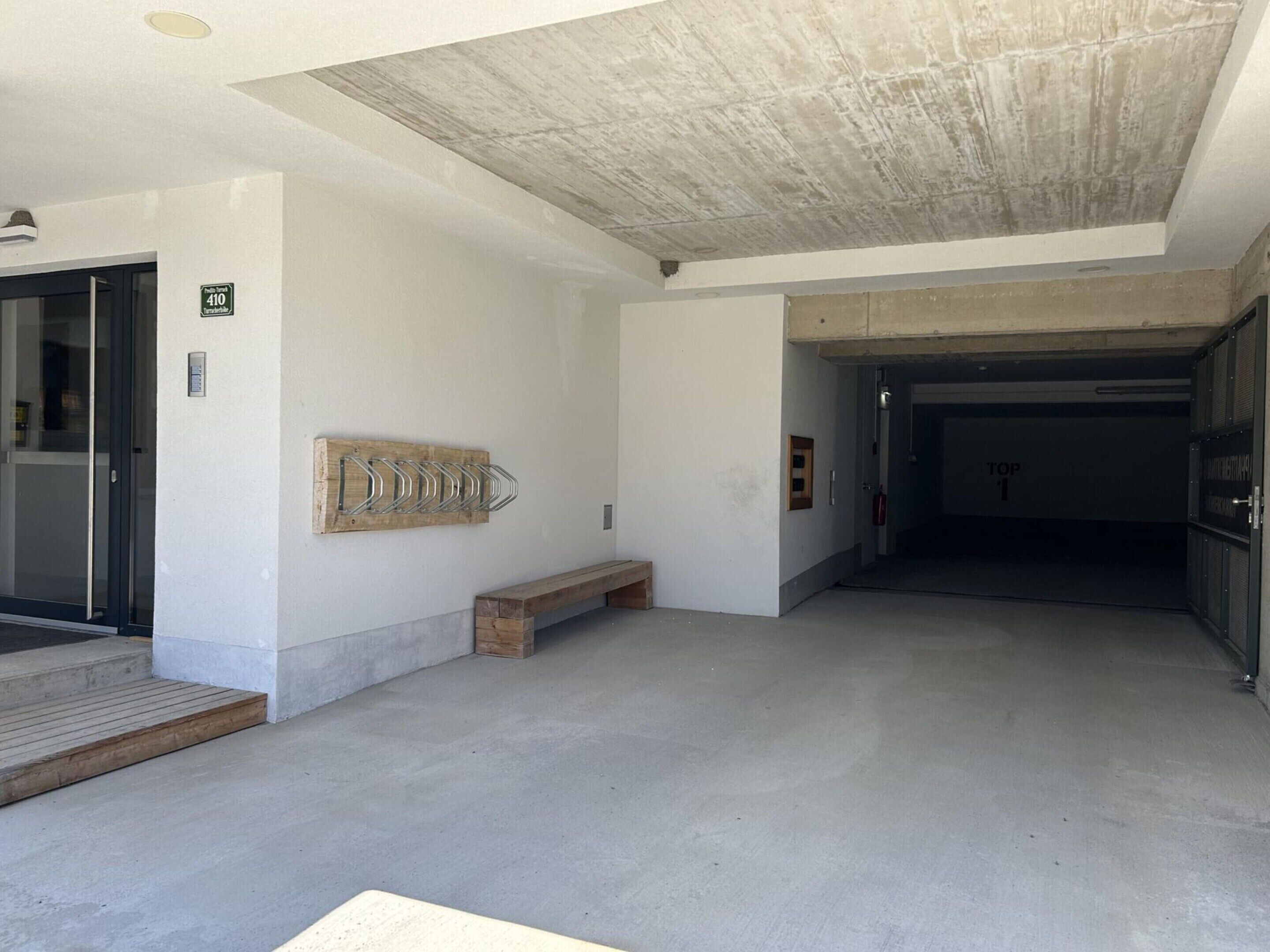 Ein geräumiger Innenraum mit Beton Decke, einer Holzbank und einem Metallregal an der Wand.