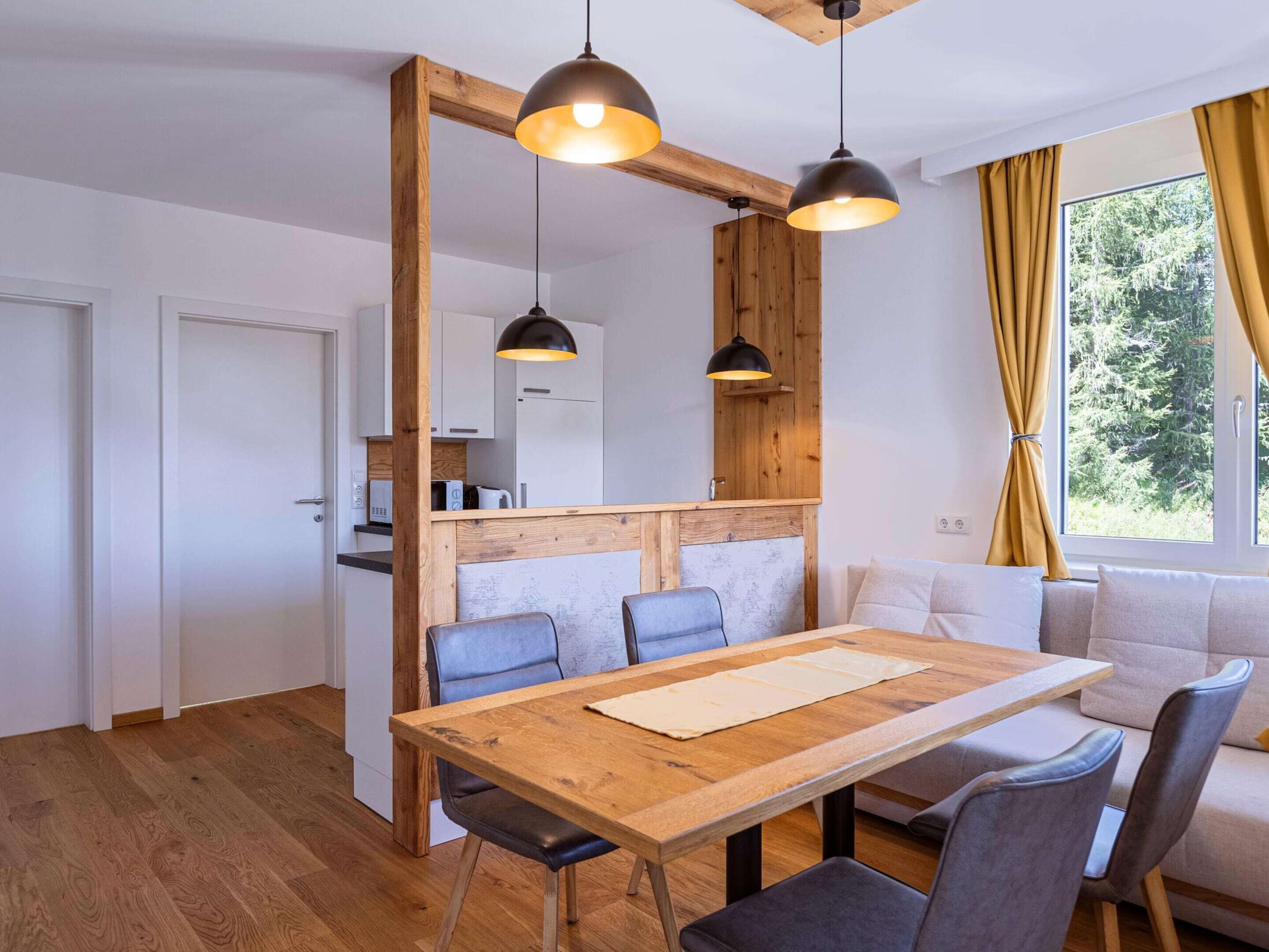 A modern kitchen with wooden accents, a dining area with a wooden table and chairs, and a sofa by a window with curtains.