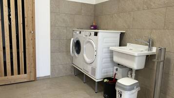 A compact laundry room with a washing machine, dryer, sink, and trash bin.