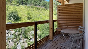 A wooden deck with a table and chairs, overlooking a green hillside with trees and shrubs. - Nice Apartment With Balcony or Terrace (Stadl-Predlitz)