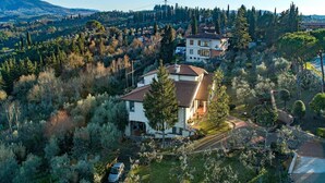 A two-story house with a tiled roof, surrounded by a garden with various trees and shrubs. - Cozy apartment nestled in the Chianti hills 10 km from Florence (Toscana)