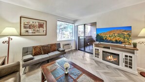 A modern living room with a sofa, coffee table, fireplace, TV, and large windows.