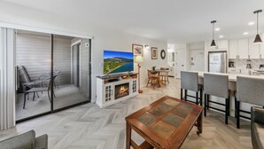 A modern kitchen with white cabinets, a dining area with a table and chairs, and a fireplace with a TV above it.
