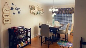 A dining area with a wooden table, chairs, and a small side table. There are wall decorations and a window with blinds. - Treasure Bay 3-bedroom house with WiFi, fitness room in Monroe  (Monroe)