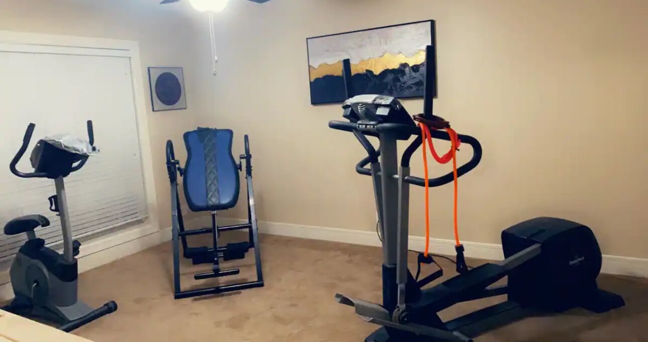 Een huisgymnasium met een elliptische trainer, een hometrainer, een gewichtbank en een loopband.