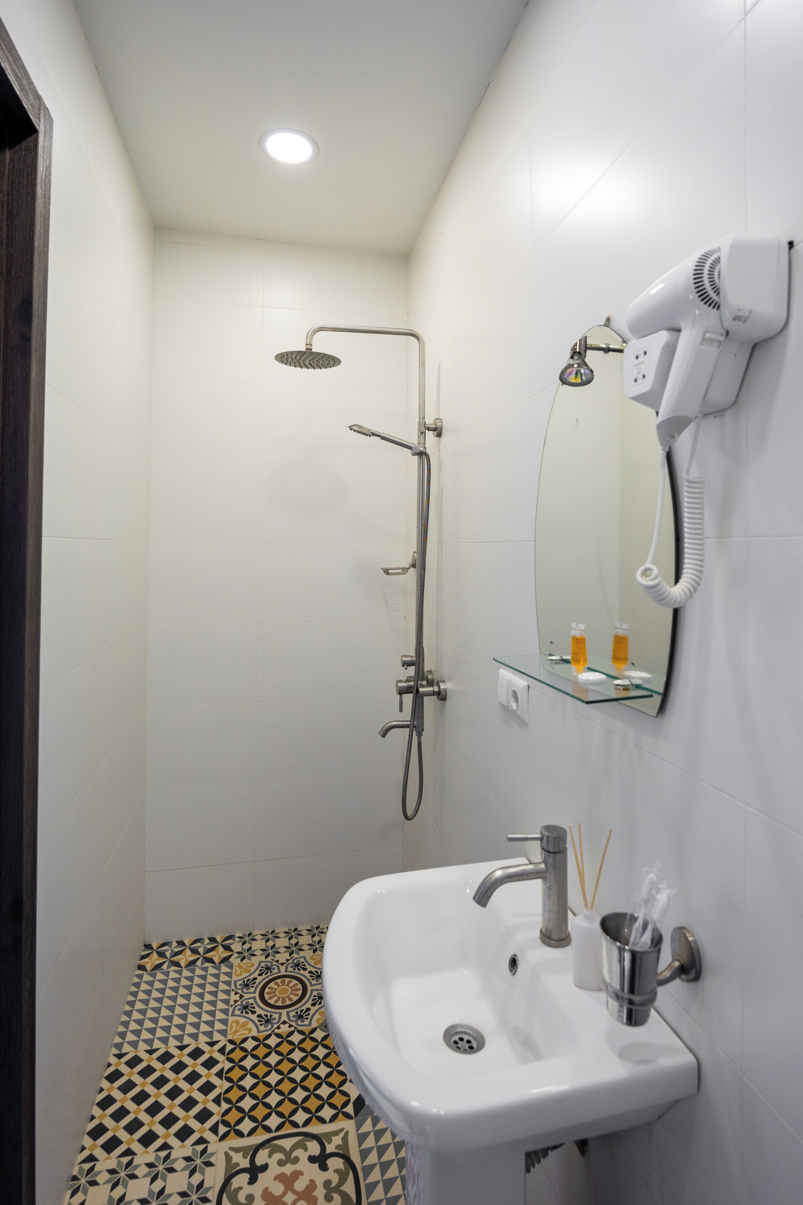 A bathroom with a shower, a sink, a mirror, and a hairdryer mounted on the wall.