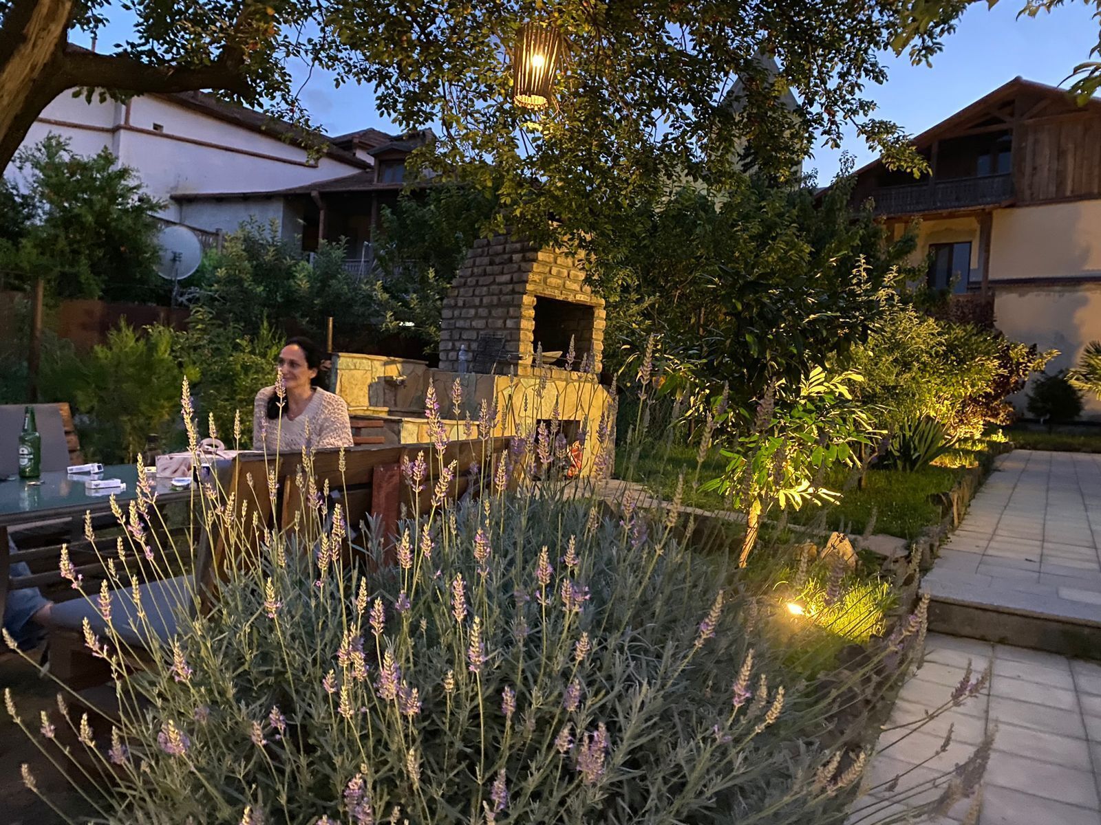 En uteplats med en stenugn, omgiven av frodig grönska och ett matbord med utomhusmöbler.