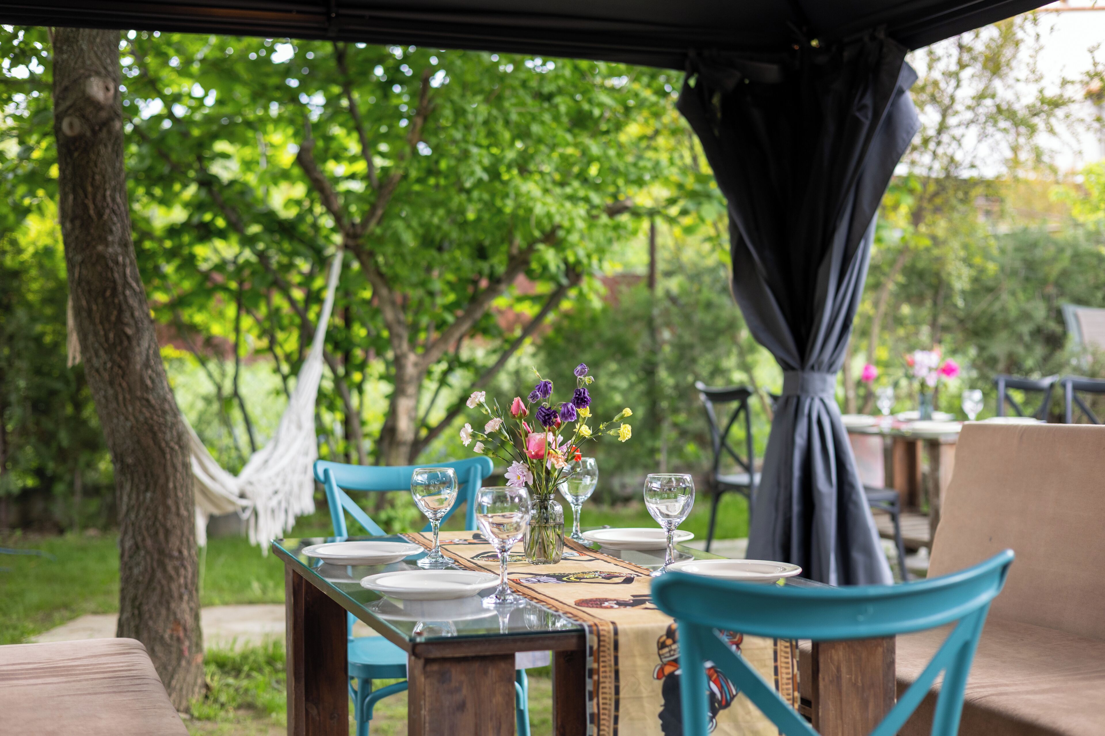 Un área de comedor al aire libre con una mesa preparada para cuatro personas, rodeada de sillas, una hamaca y un dosel.