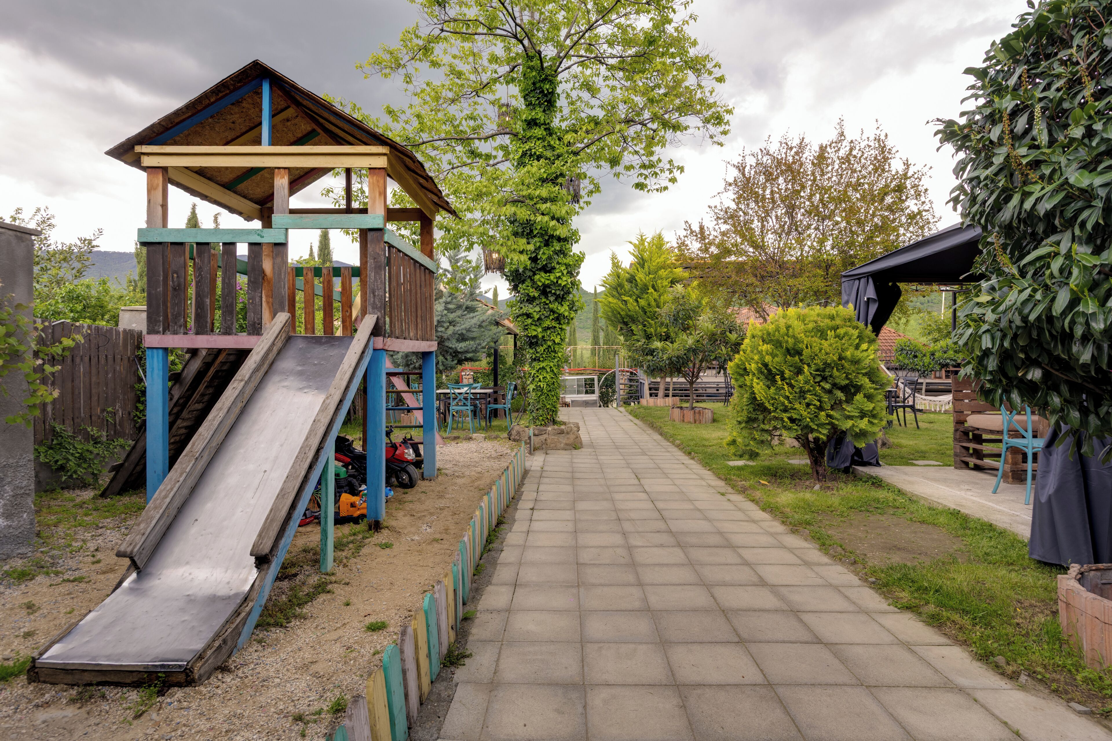 Un espace de jeux avec un toboggan et une zone d’escalade, un chemin pavé et de la verdure tout autour.