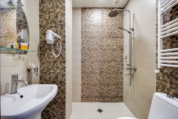 A bathroom with a sink, a toilet, a shower with a rain showerhead, and a towel rack.