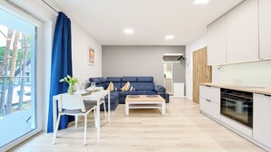 A modern living room with a blue sofa, a dining table with chairs, and a kitchen area with a stove. - Apartamenty Sun & Snow Horizon Park II (Dziwnów)