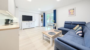A modern living room with a blue sofa, a wooden coffee table, and a TV in the background. - Apartamenty Sun & Snow Horizon Park II (Dziwnów)