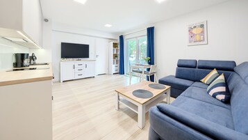 Una sala de estar moderna con un sofá azul, una mesa de centro de madera y un televisor al fondo.