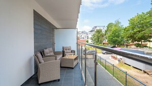 A balcony with wicker furniture and a glass door, overlooking a street with buildings and trees. - Apartamenty Sun & Snow Horizon Park II (Dziwnów)