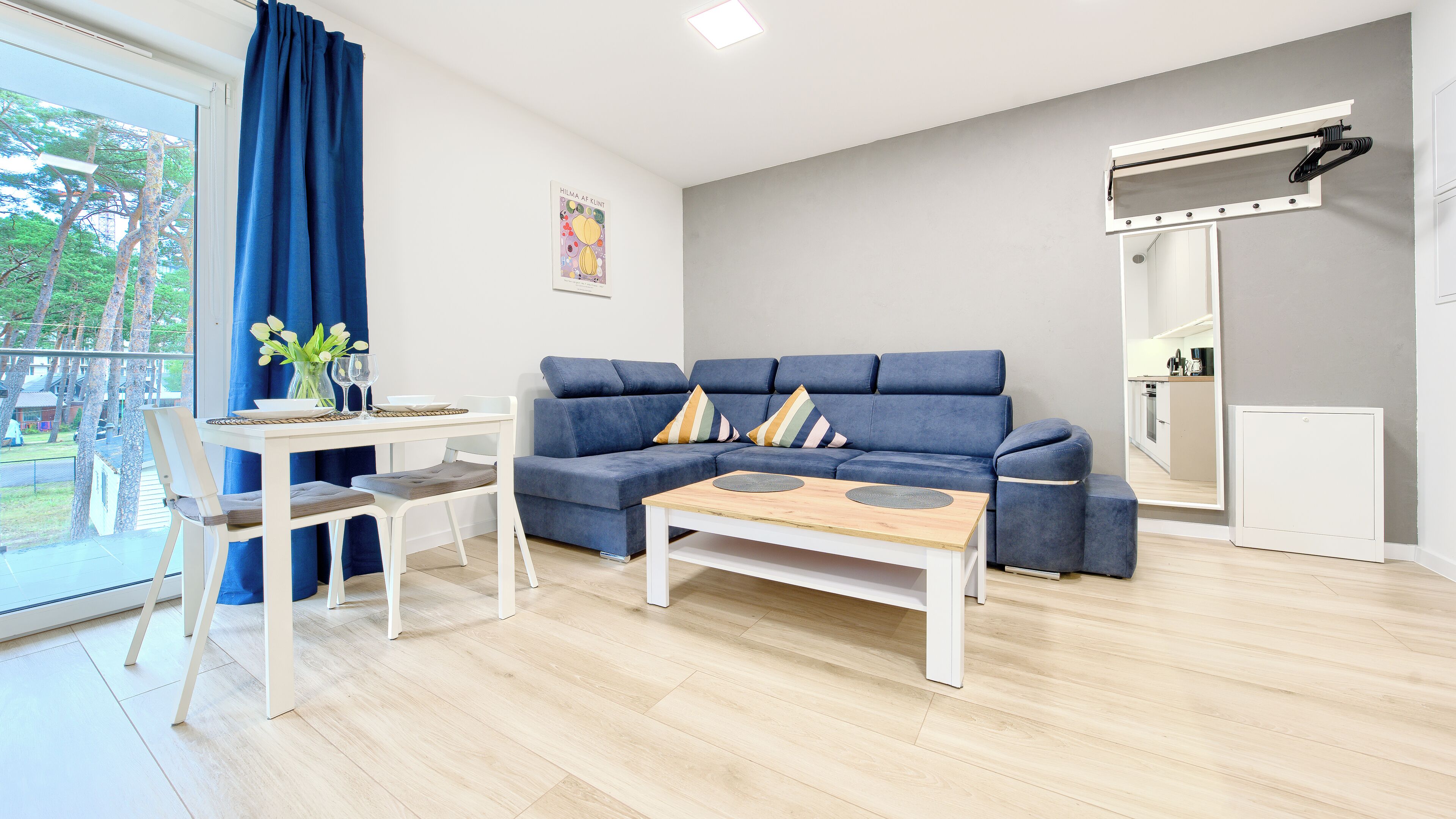 Ein modernes Wohnzimmer mit einem blauen Sofa, einem weißen Couchtisch und einem Essbereich mit Tisch und Stühlen.