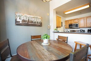 A dining area with a round wooden table, four chairs, a potted plant, and a wall-mounted sign.