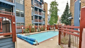 A swimming pool with a blue slide, surrounded by a red fence, and adjacent to a building with blue siding and multiple balconies. - River Mountain Lodge Aspen Trail Condo: Ski In, Downtown Breck (Breckenridge)