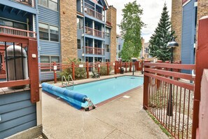 Une piscine avec un toboggan bleu, entourée d’une clôture rouge, et située à côté d’un bâtiment aux bardages bleus et doté de plusieurs balcons.