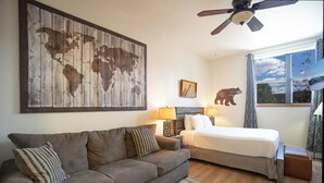 Une chambre à coucher comprenant un lit, un canapé, une œuvre d’art représentant une carte du monde, un ventilateur de plafond et une fenêtre donnant sur le ciel.
