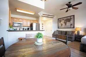 Una cocina moderna con armarios de madera, una mesa de comedor con un centro de mesa con planta y un ventilador de techo.