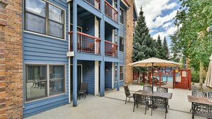 A multi-story building with a blue exterior, a balcony with red railings, and outdoor seating with a table and chairs. - River Mountain Lodge Aspen Trail Condo: Ski In, Downtown Breck (Breckenridge)
