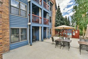 Un immeuble à plusieurs étages, à la façade bleue, doté d’un balcon avec des balustrades rouges et d’un espace extérieur aménagé avec une table et des chaises.