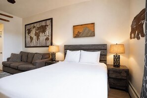 A hotel room with a large bed, two nightstands, a sofa, and two wall-mounted lamps.