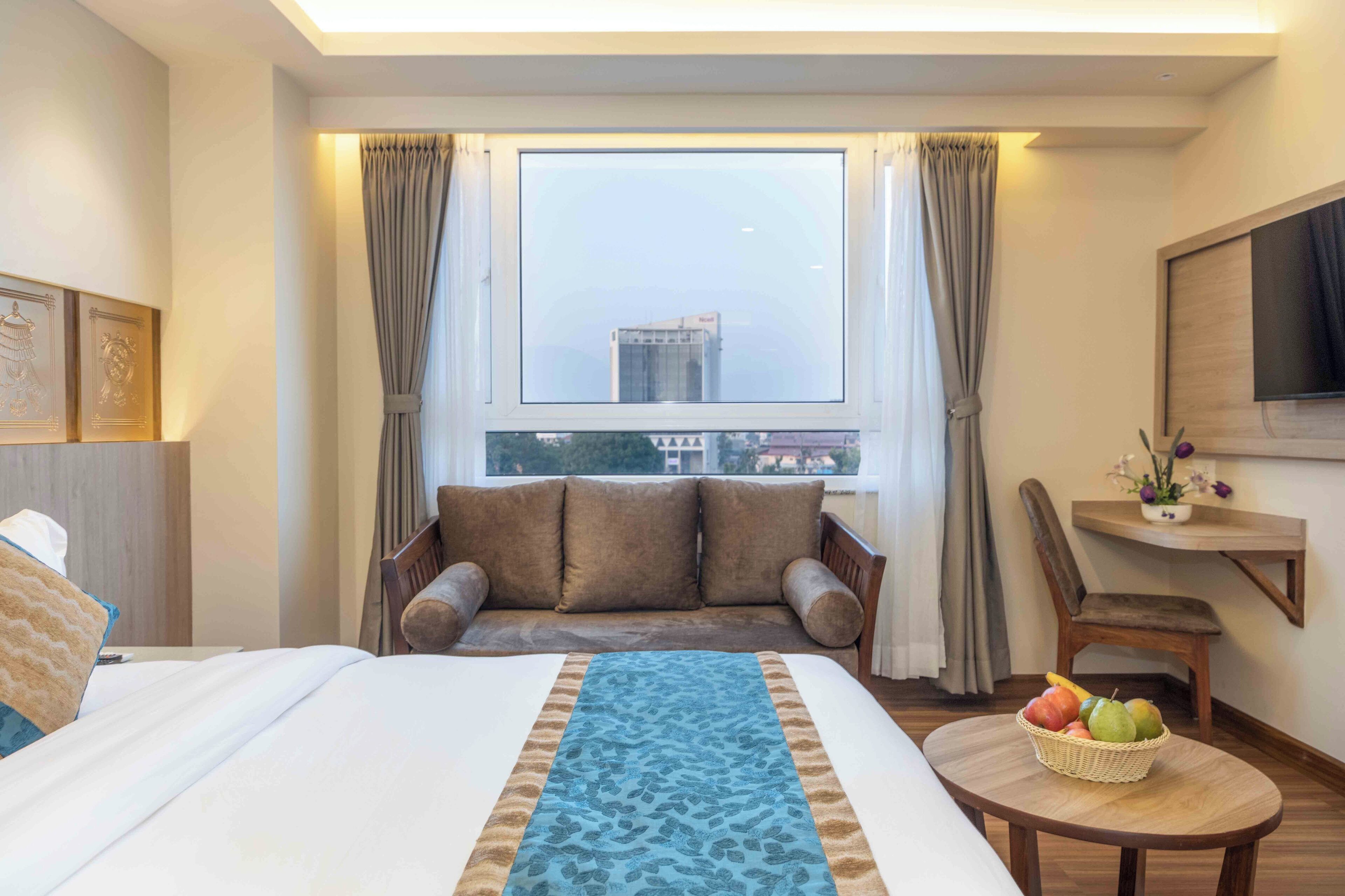 Une chambre d’hôtel avec un lit, un canapé, une petite table avec des fruits et un téléviseur fixé au mur.