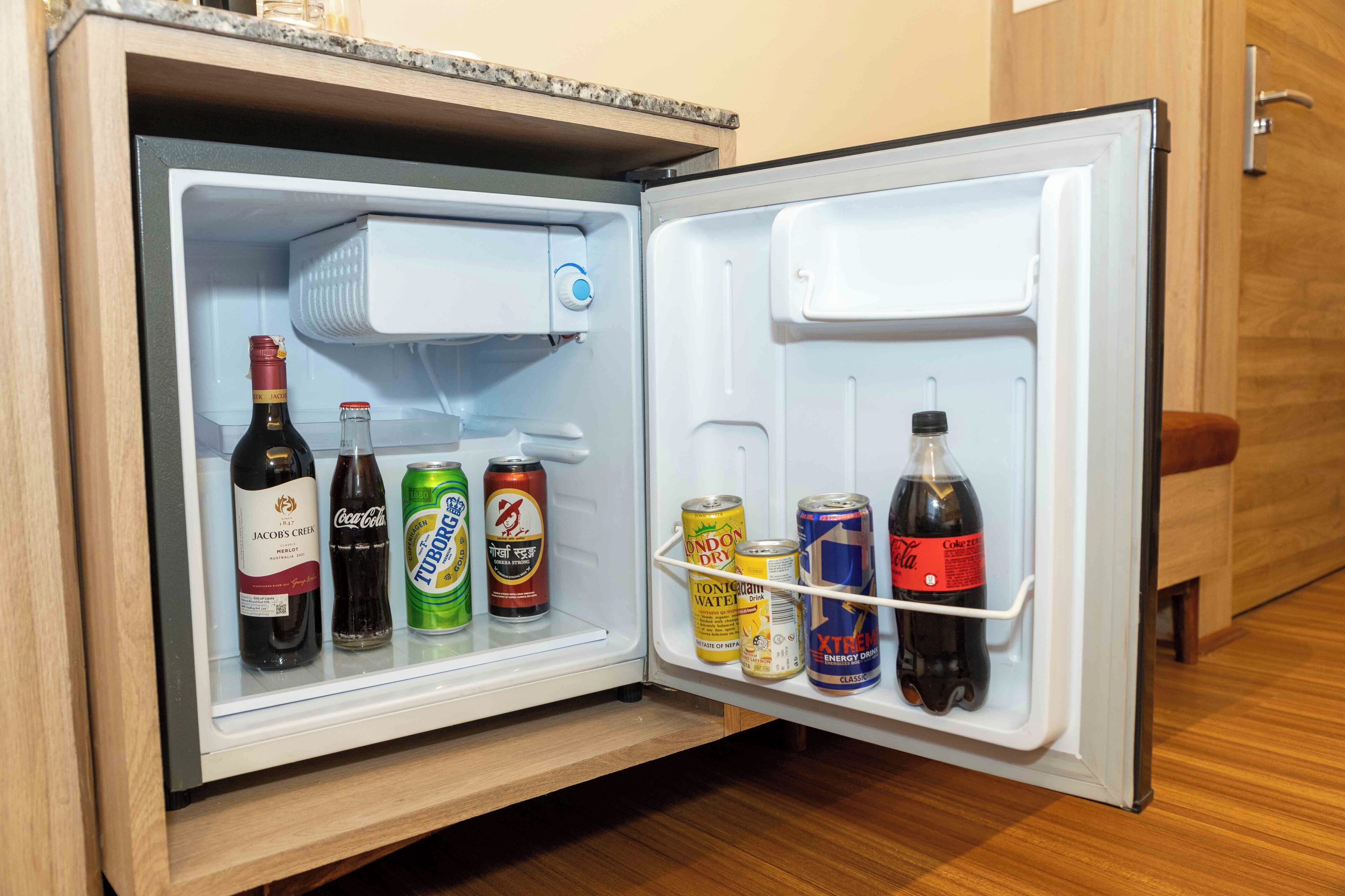 A small refrigerator with a freezer compartment on top, containing various beverages and cans.