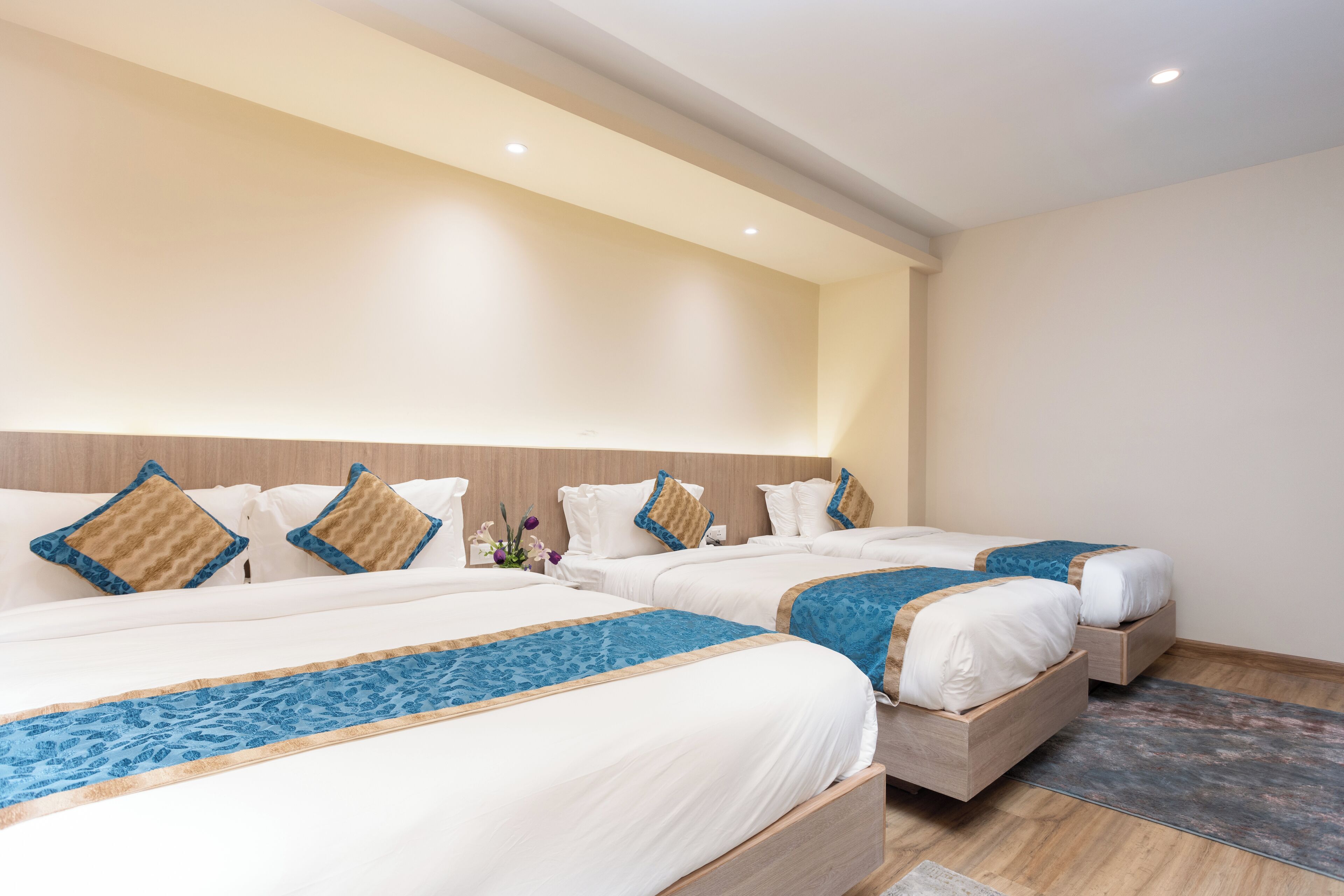 A hotel room with three single beds, each with a blue and white bedspread and matching pillows.