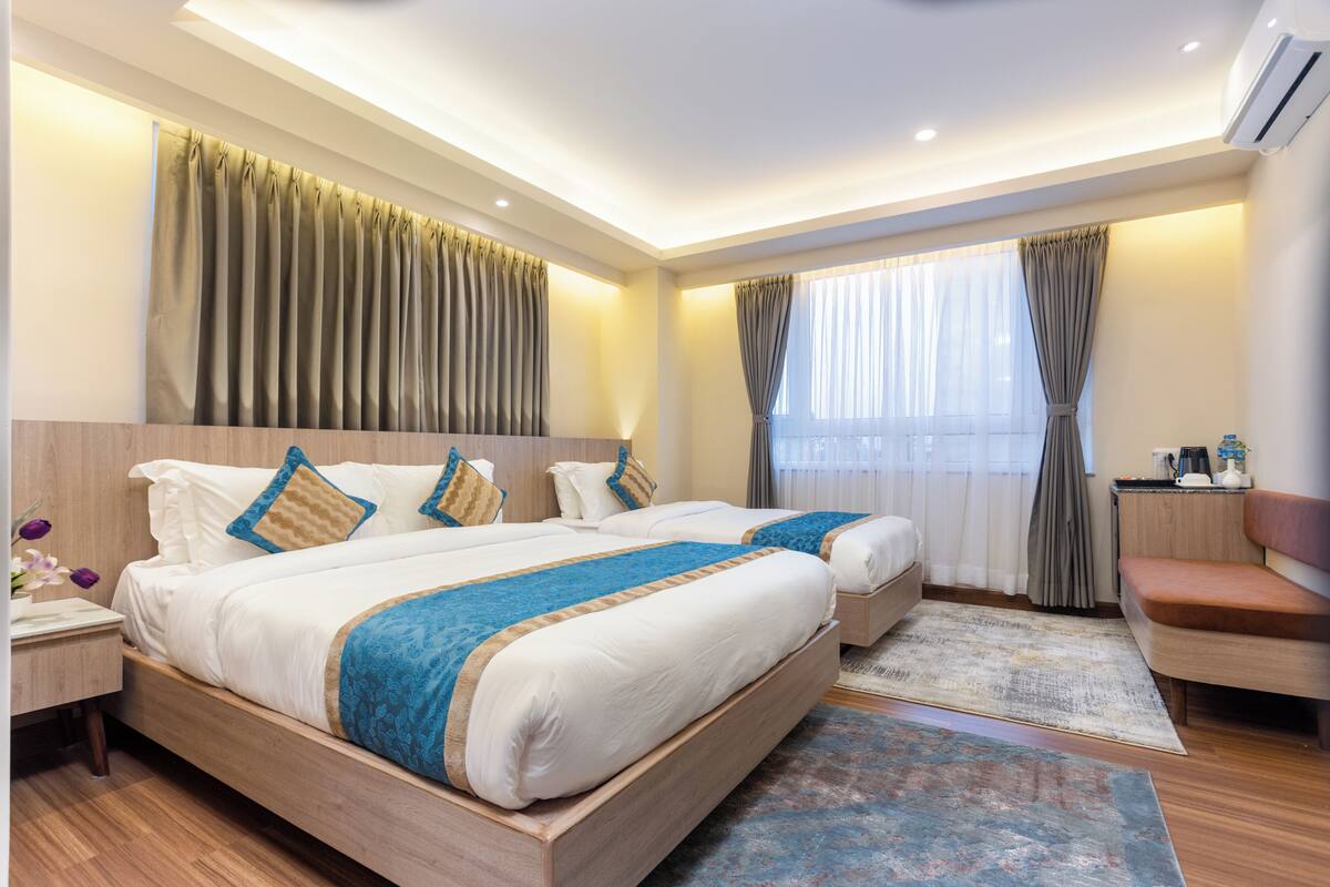 A hotel room with two beds, a desk, a chair, and a large window with curtains.